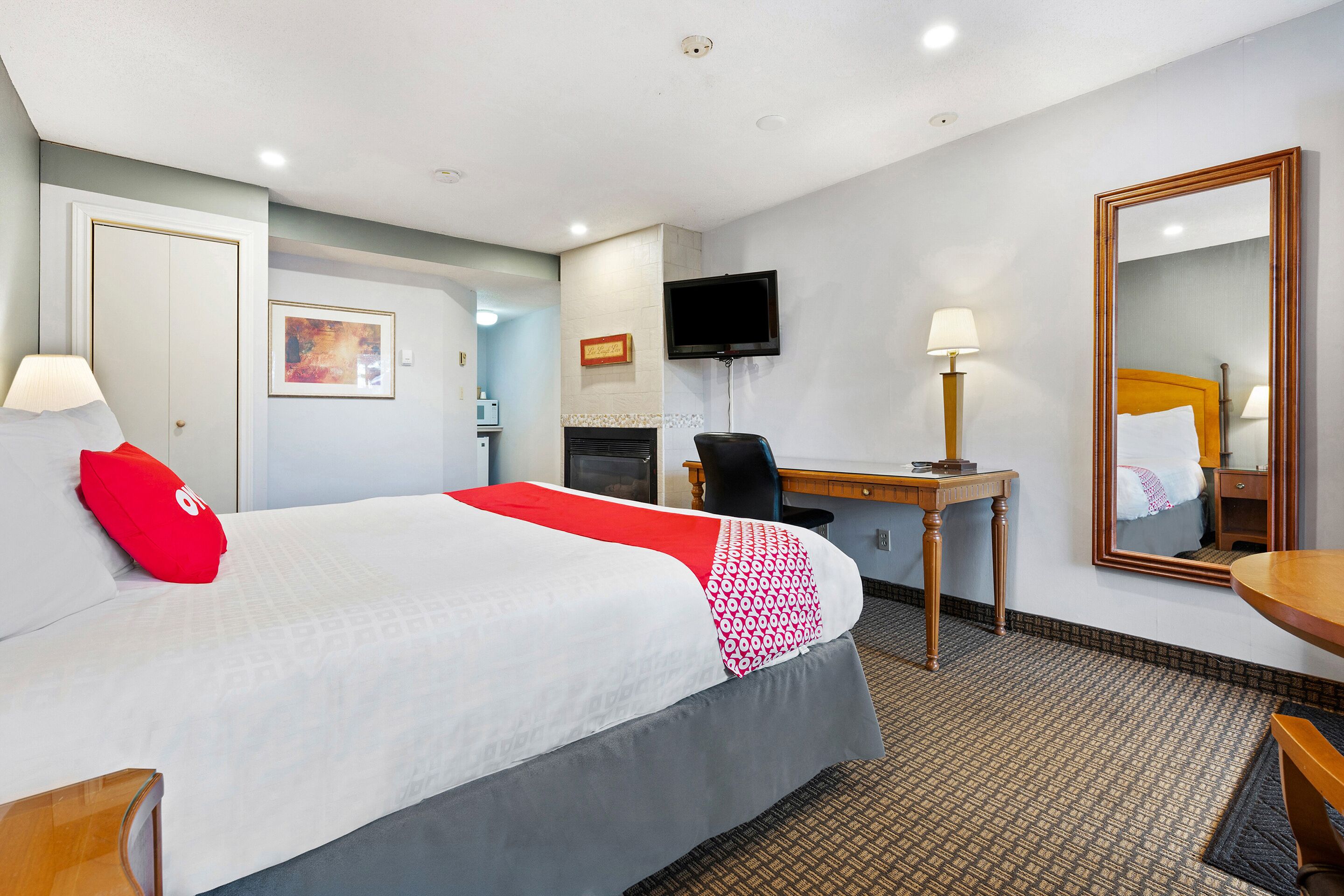 A hotel room with a bed, desk, chair, TV, and a mirror.