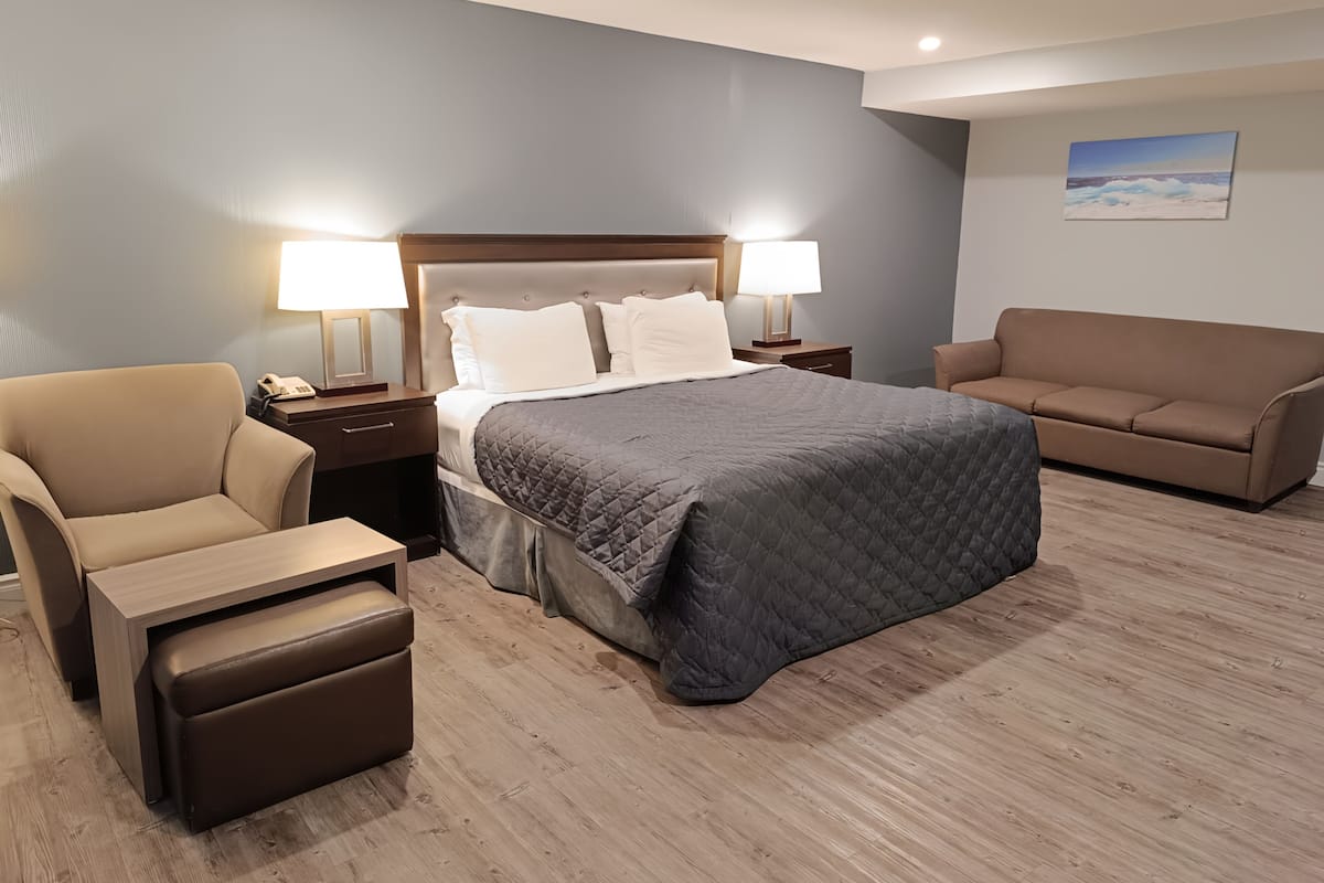 Ein Hotelzimmer mit einem Bett, zwei Nachttischlampen, einem braunen Ledersessel, einem braunen Sofa und Holzboden.