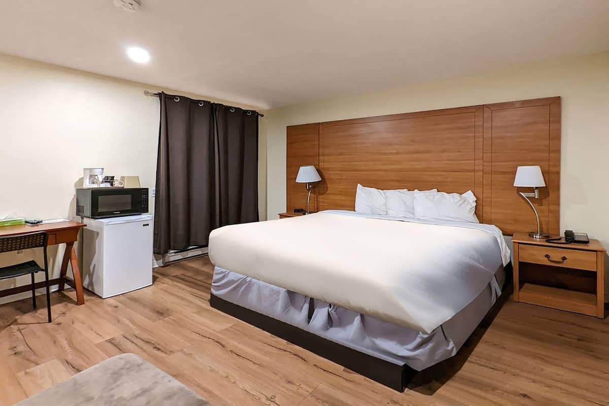 Ein Hotelzimmer mit einem Bett, einem Schreibtisch mit Mikrowelle, einem kleinen Kühlschrank, zwei Nachttischlampen und einem hölzernen Kopfteil.