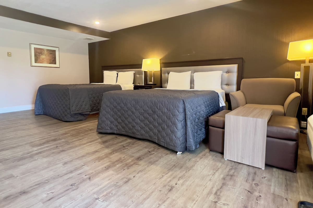 Ein Hotelzimmer mit zwei Betten, einem Sessel und einem Nachttisch mit Lampe.
