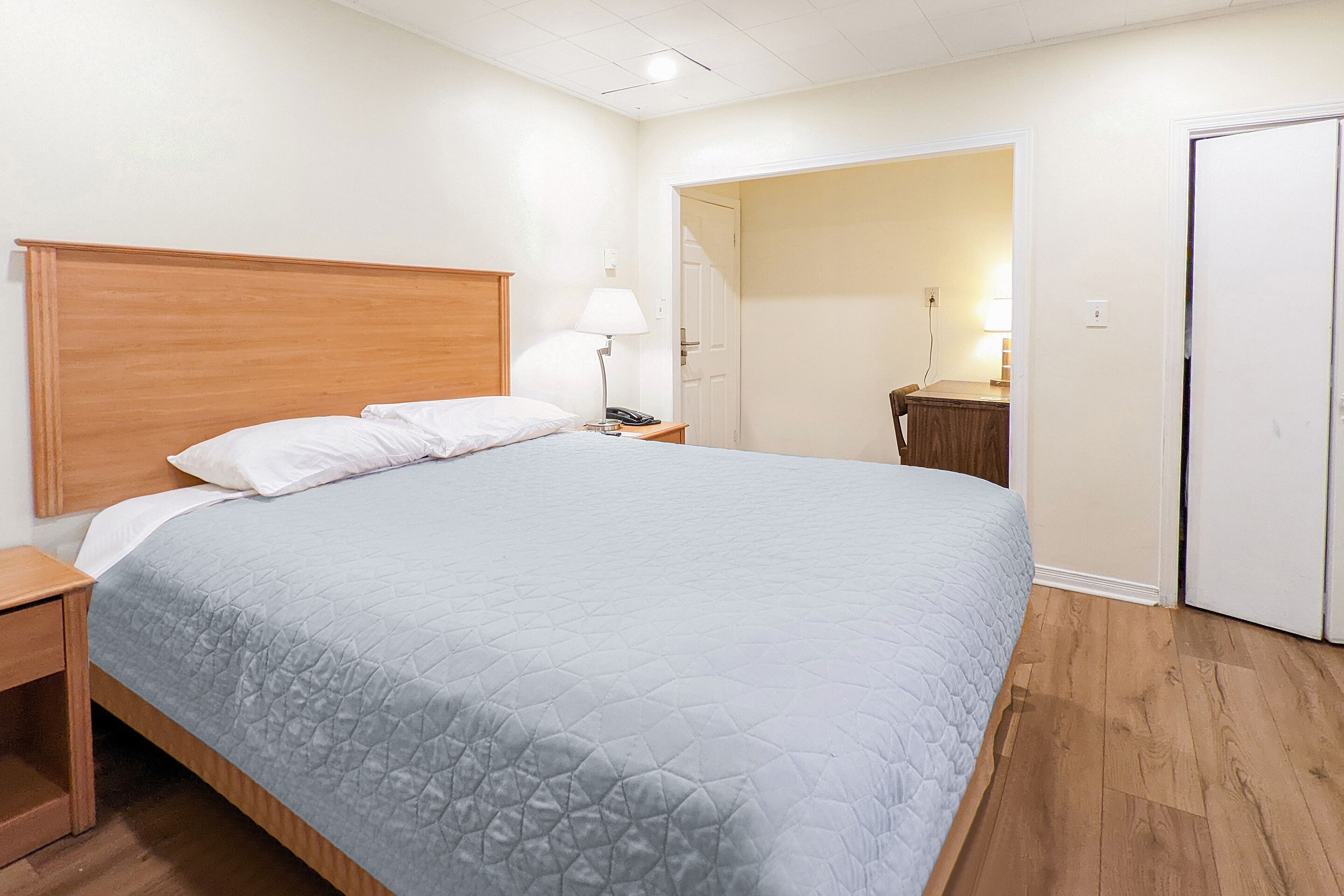A bedroom with a large bed, a nightstand, a bedside lamp, and a wooden headboard.