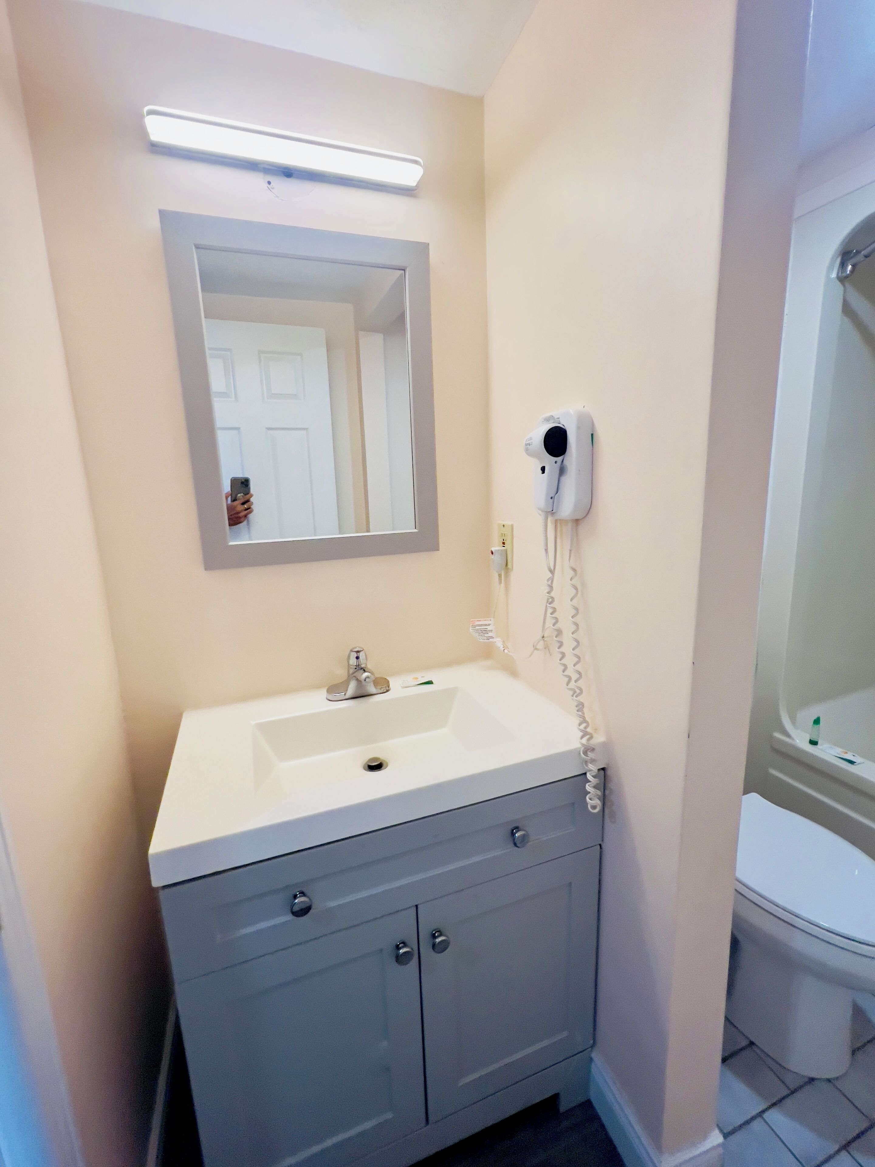 A bathroom with a white sink, a mirror, a hairdryer, and a toilet.