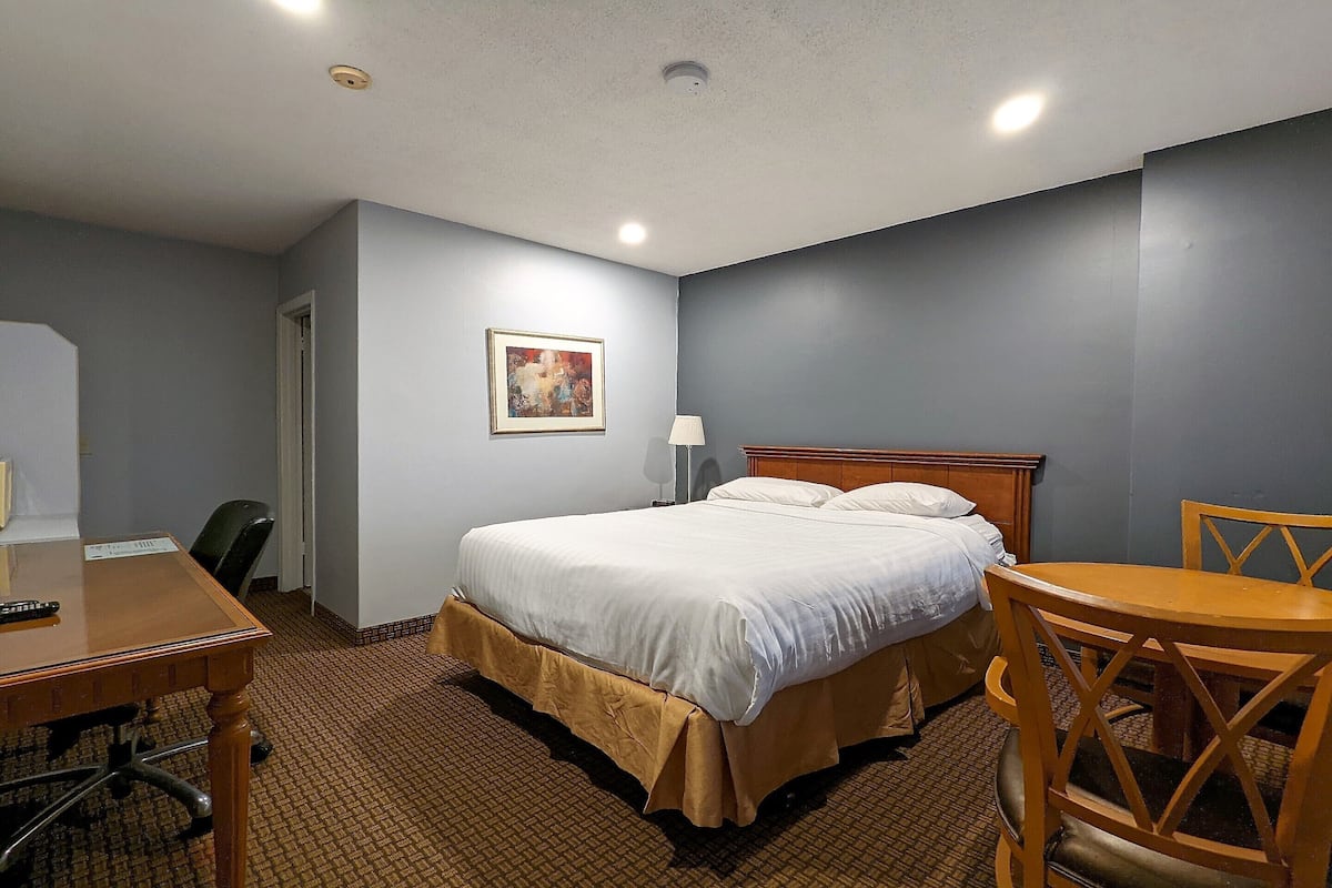 Ein Hotelzimmer mit Bett, Schreibtisch, Stuhl, Lampe und einem Bild an der Wand.