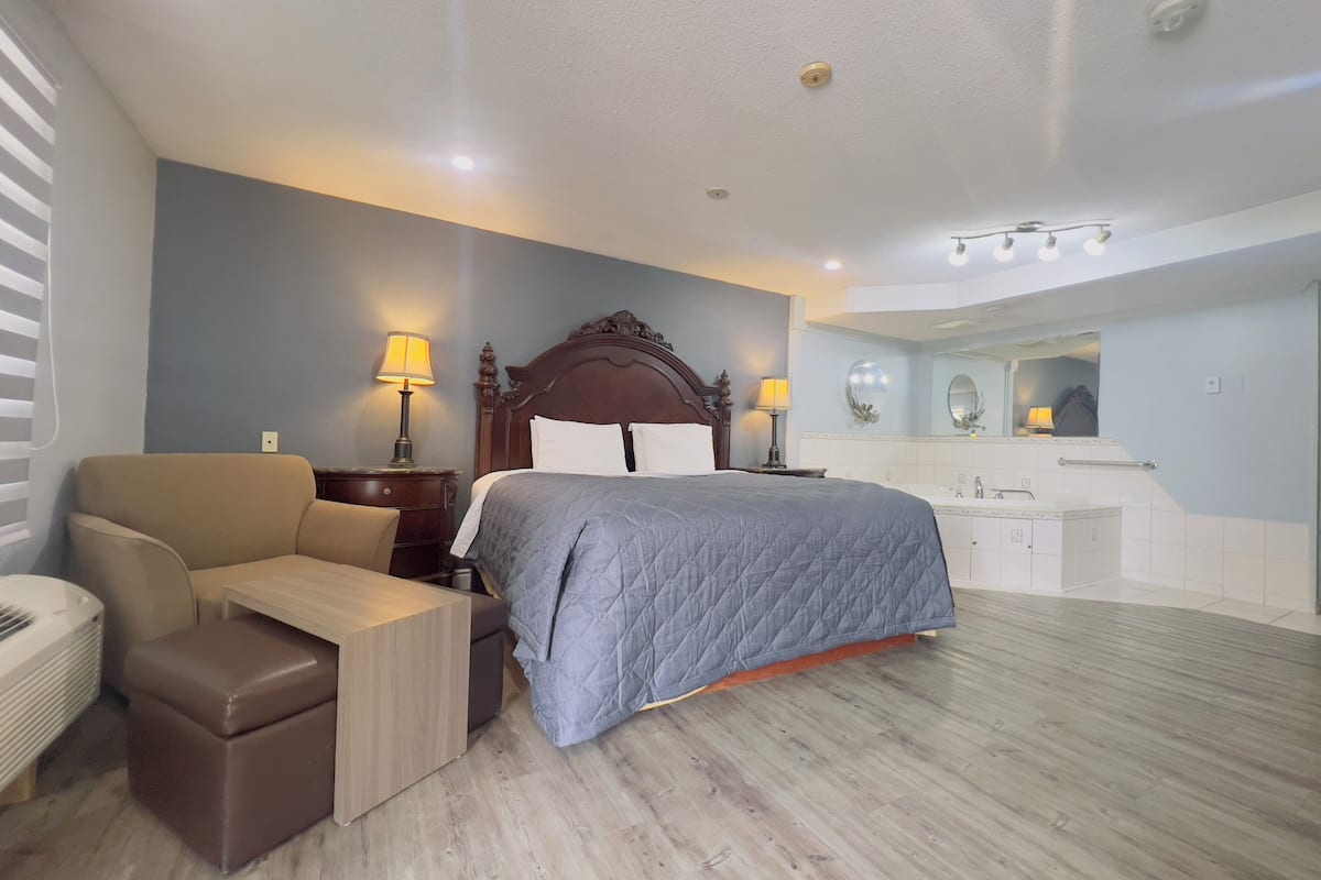 Ein Hotelzimmer mit Bett, Schreibtisch, Stuhl, Kommode und einem Badezimmer mit Spiegel und Waschbecken.