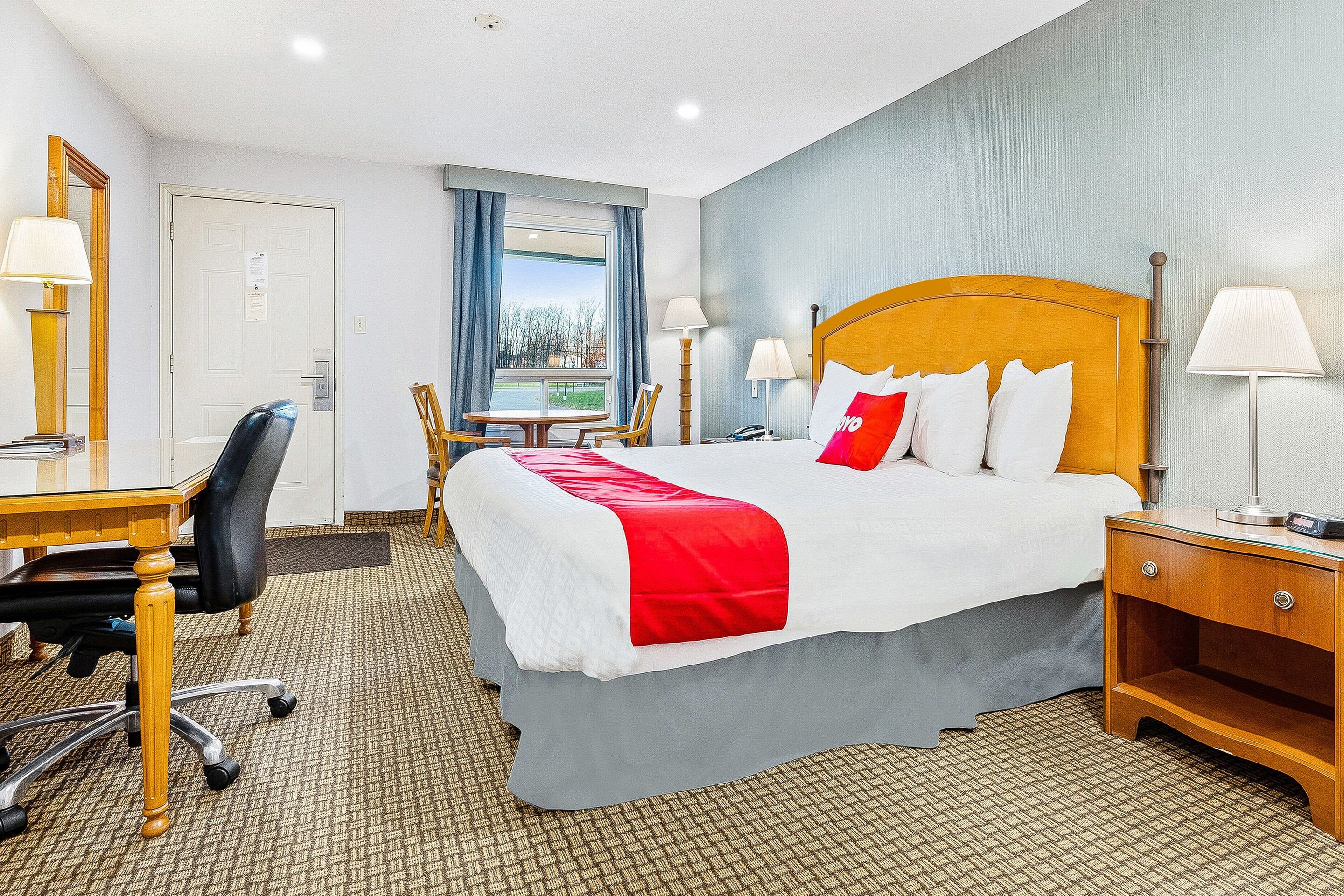 A hotel room with a bed, desk, chair, and a view of the outdoors.