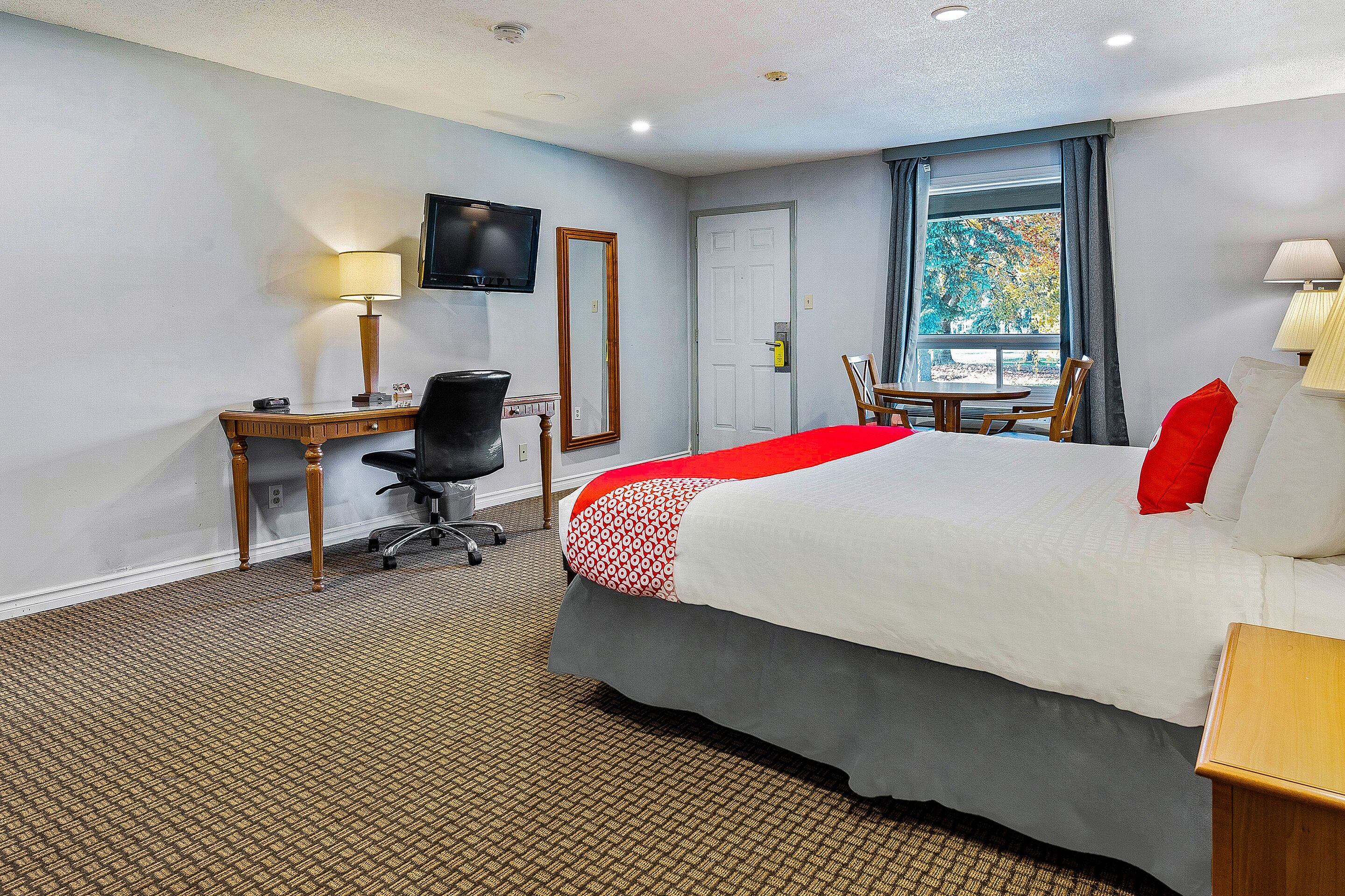 A hotel room with a bed, desk, chair, TV, and a window with a view.