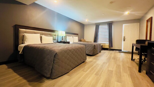 Une chambre d  ’hôtel avec deux lits, un bureau, une chaise, une lampe et une fenêtre avec des stores.
