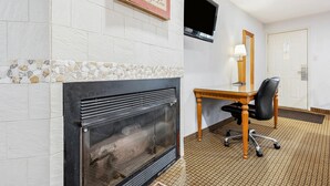 Une pièce avec une cheminée, un téléviseur fixé au mur, un bureau en bois avec une chaise, et une porte au fond.