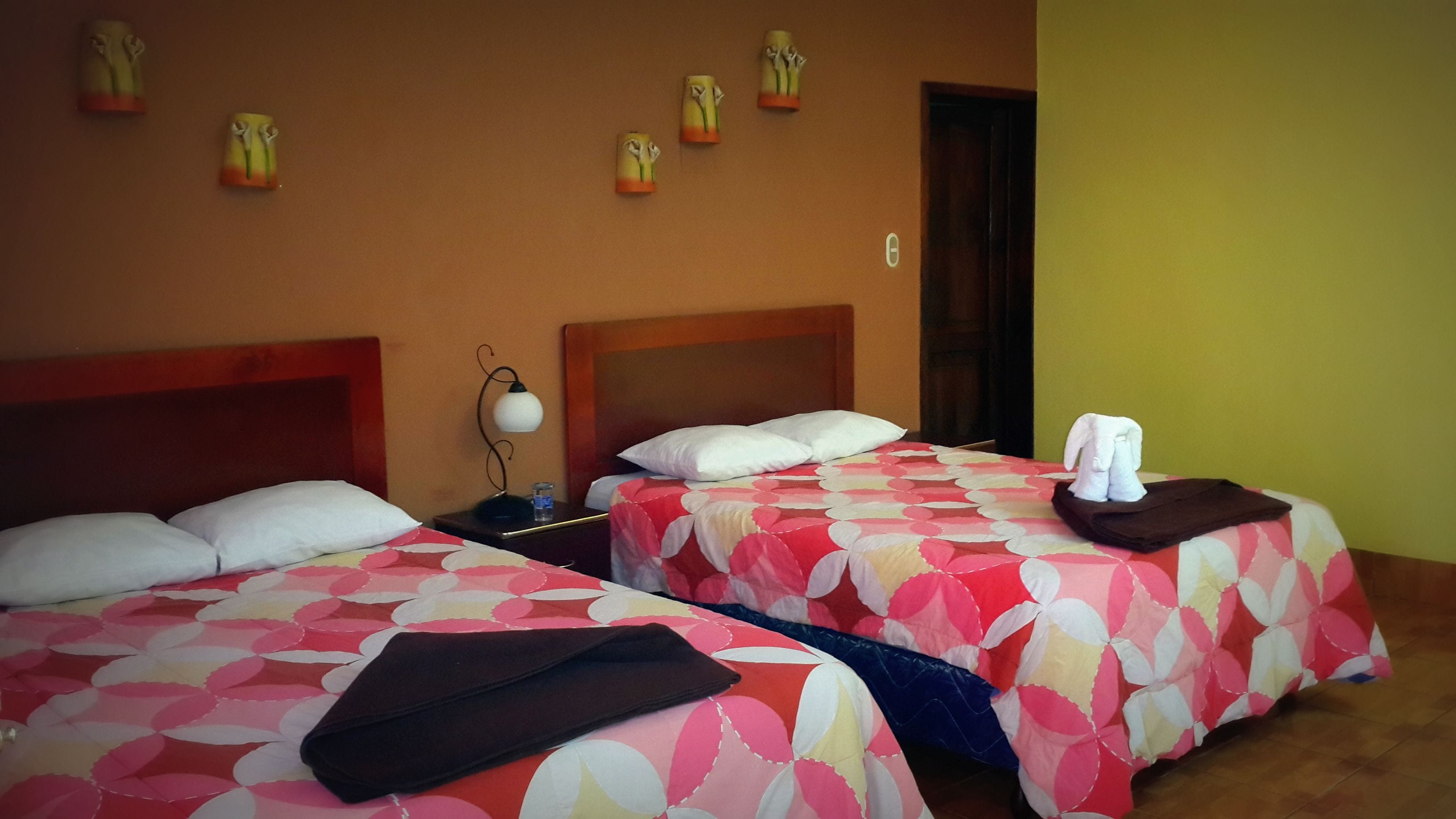 Une chambre d’hôtel avec deux lits, chacun recouvert d’une couvre-lit à motifs floraux, une table de chevet avec une lampe et une serviette sur chaque lit.