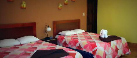 Une chambre d’hôtel avec deux lits, chacun recouvert d’une couvre-lit à motifs floraux, une table de chevet avec une lampe et une serviette sur chaque lit.
