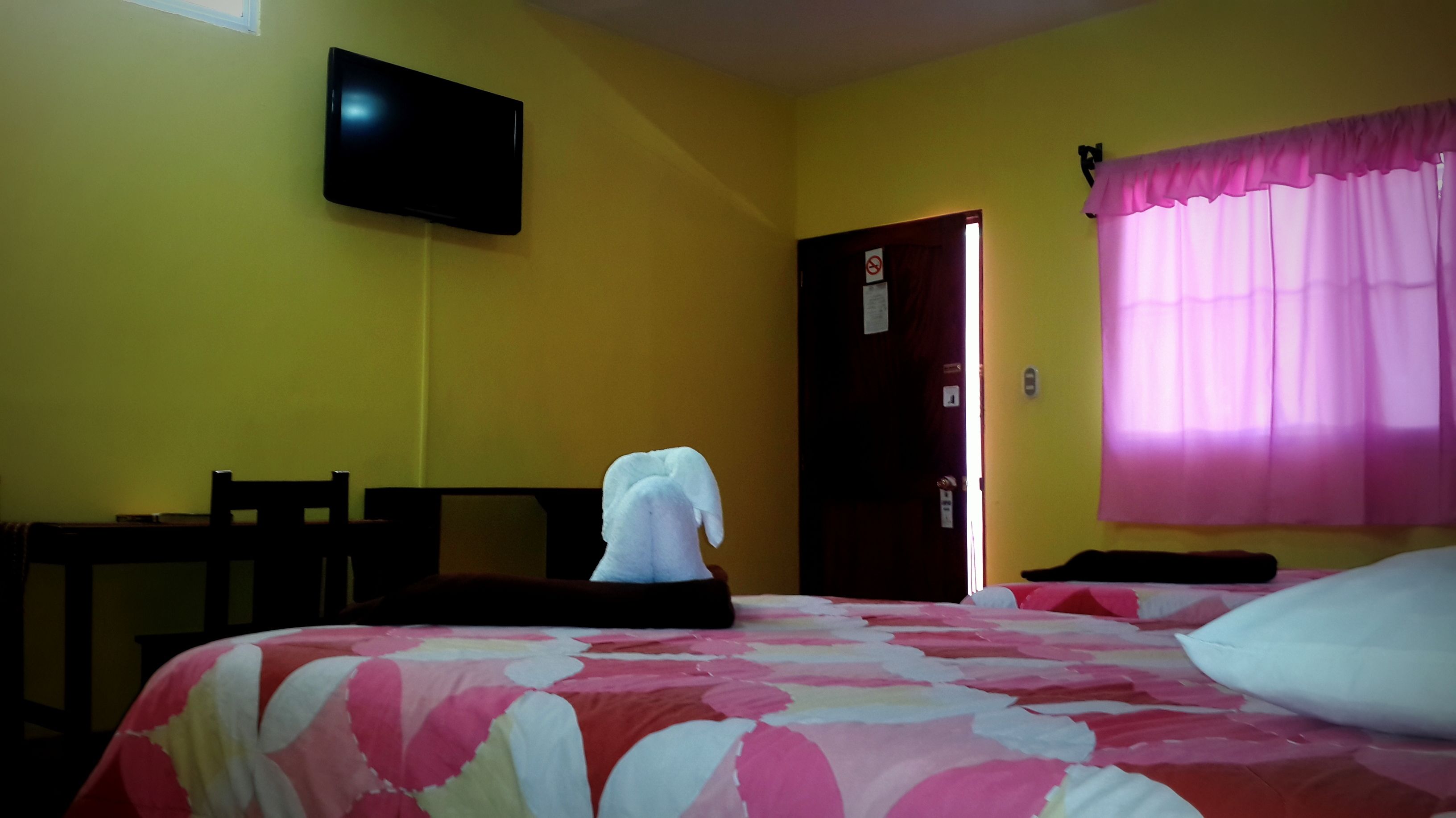 Ein Hotelzimmer mit einem Bett, einem Sessel, einem an der Wand montierten Fernseher und einer Tür.