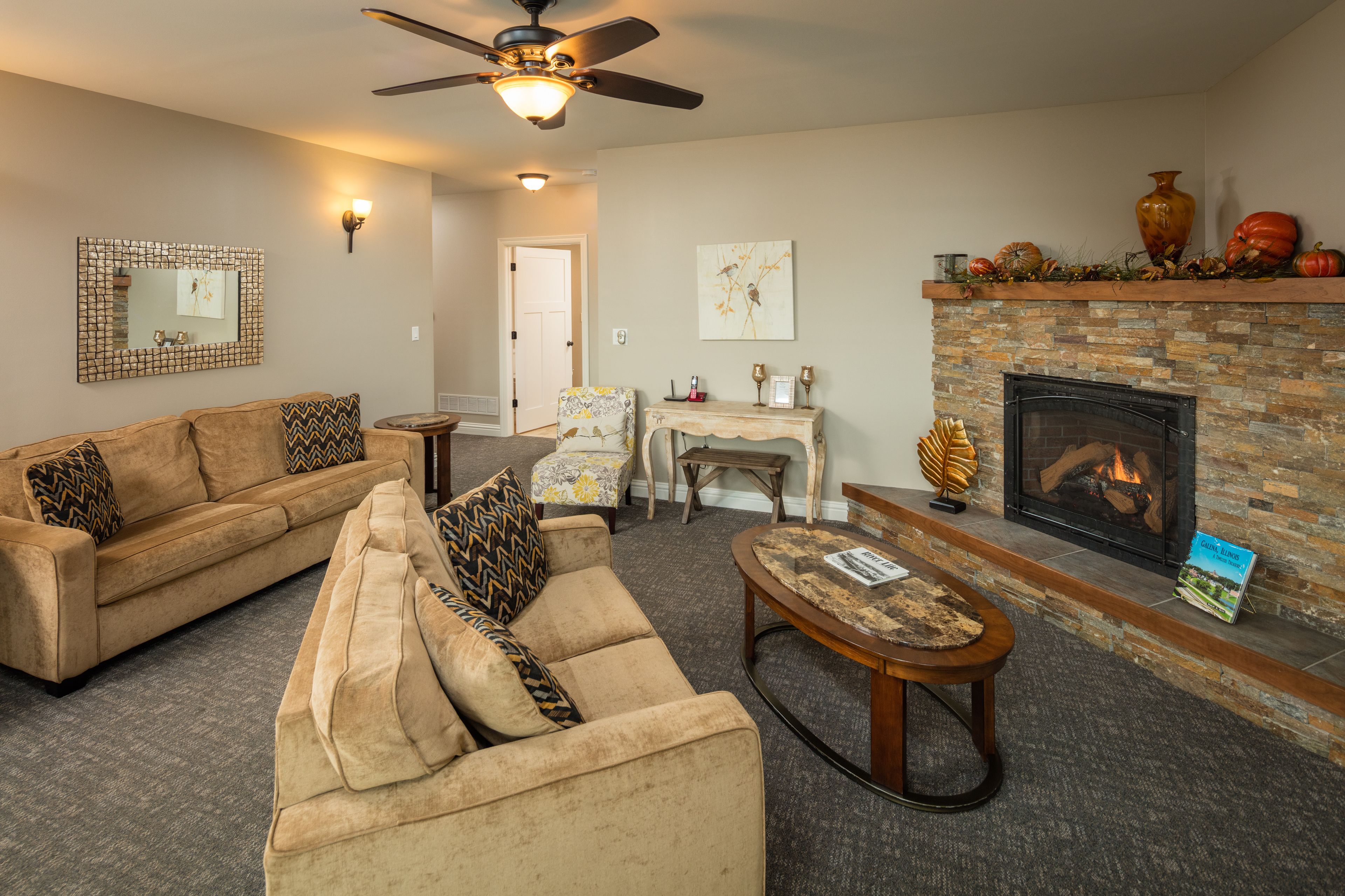 A living room with a fireplace, a sofa set, a coffee table, and a ceiling fan.