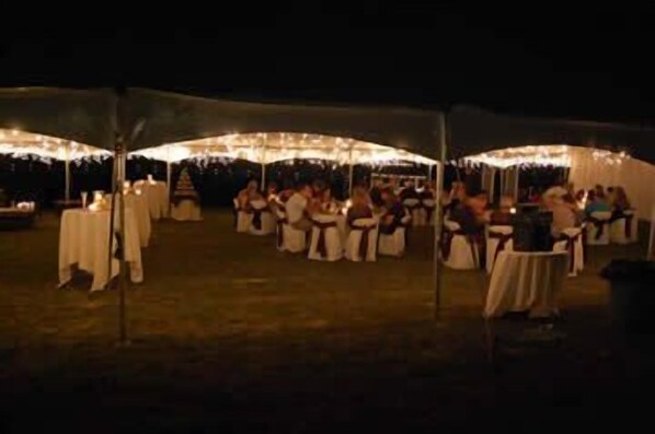 An outdoor event with tables covered in white tablecloths and people seated under string lights.