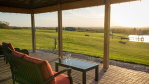 An outdoor patio with a wooden bench and table, a view of a grassy field, and a distant body of water. - Lefevre Inn and Resort (Galena)