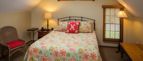 A bedroom with a bed, a chair, a nightstand, a lamp, a window, and a wooden bench.