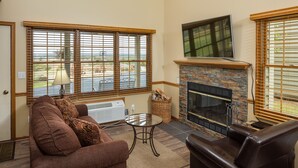 A living room with a fireplace, a sofa, a coffee table, and large windows with blinds. - Lefevre Inn and Resort (Galena)