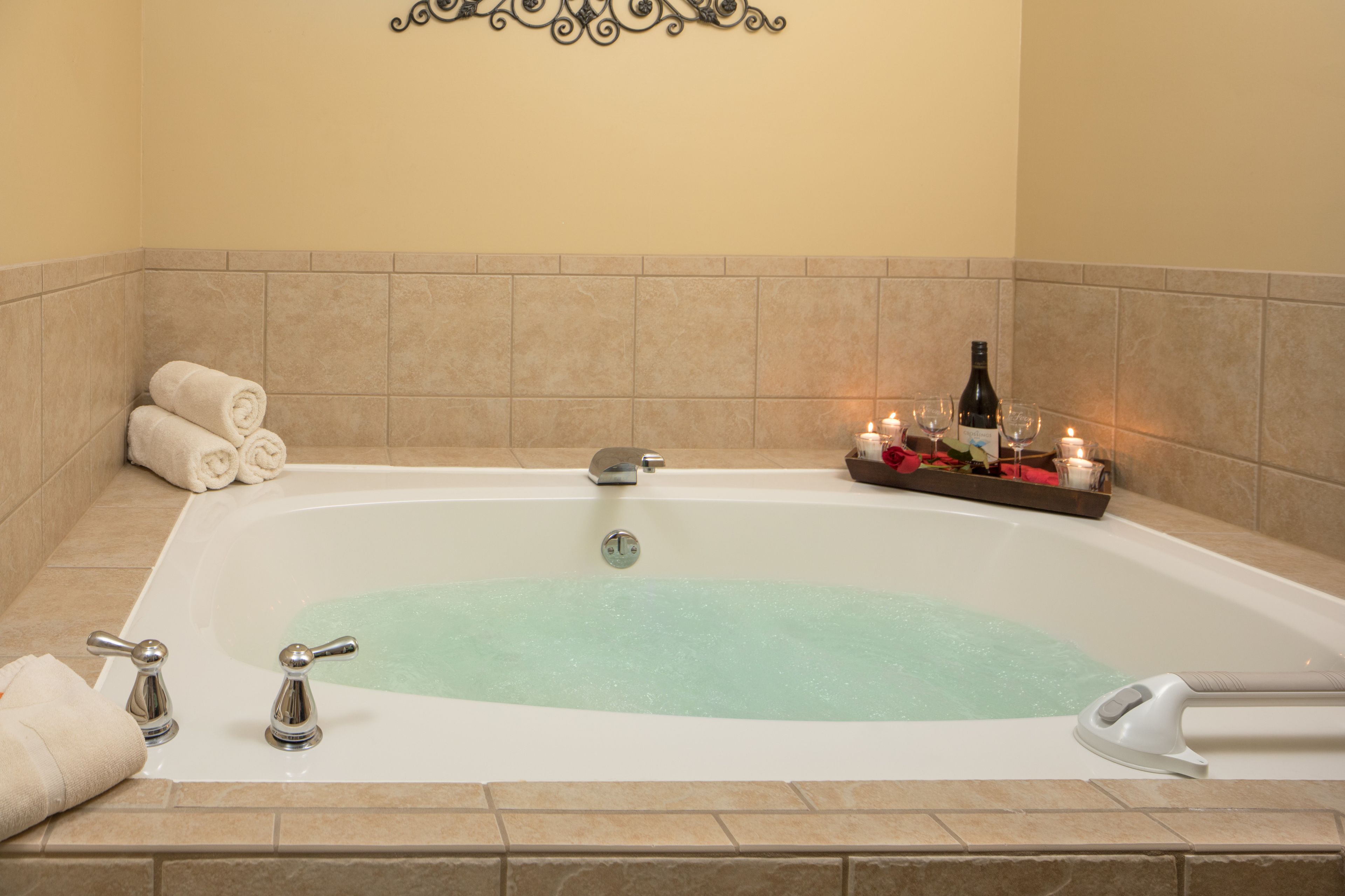 A bathtub with a greenish water feature, two faucets, and a bottle of wine and candles on the side.