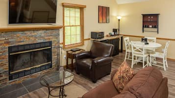 A living room with a fireplace, leather sofa, and a dining area with white chairs.