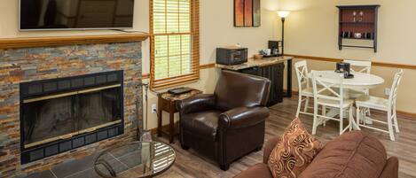 A living room with a fireplace, leather sofa, and a dining area with white chairs.