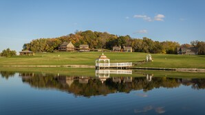 A tranquil lakeside scene with a gazebo, a small bridge, and houses in the background. - Lefevre Inn and Resort (Galena)