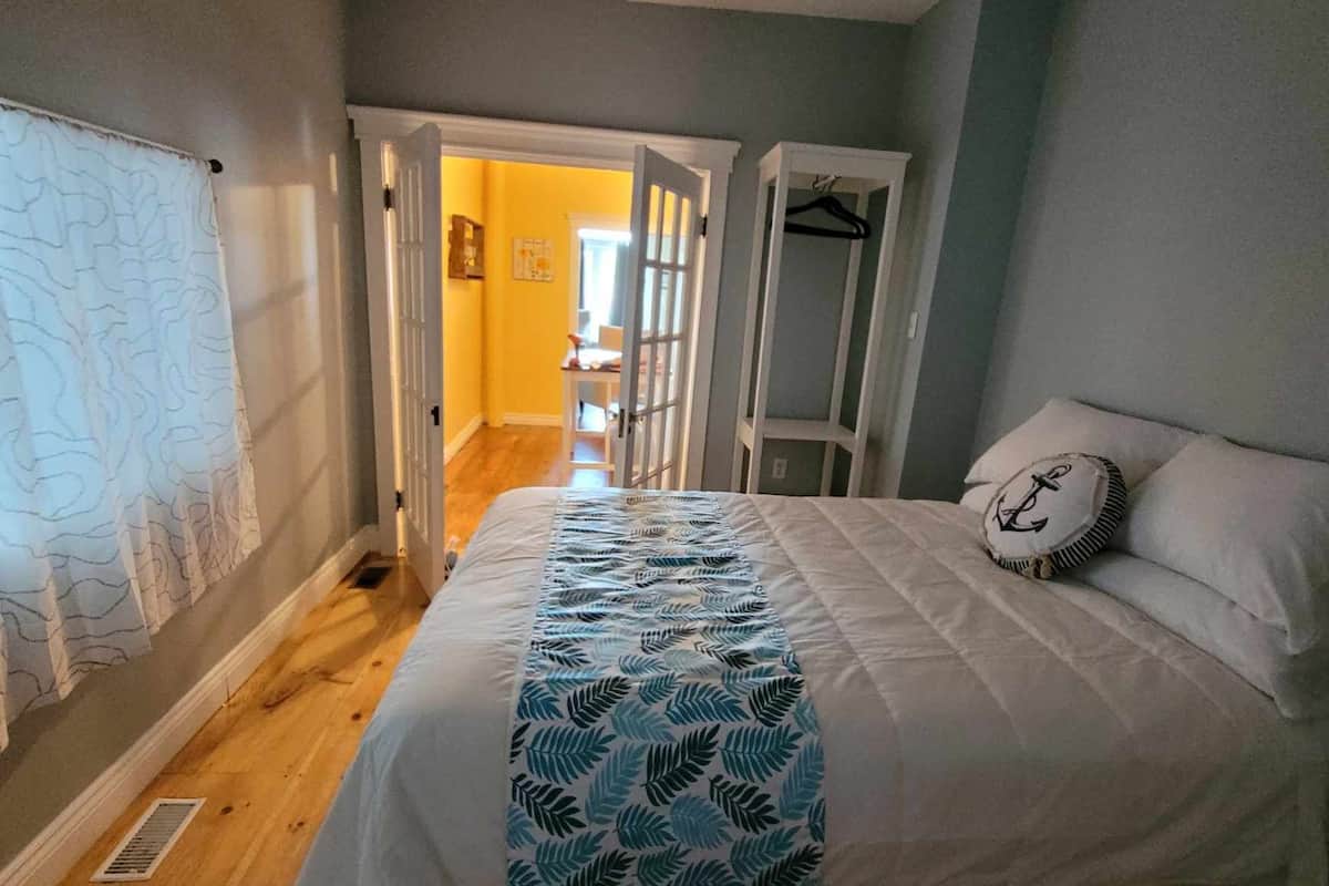 Ein Schlafzimmer mit einem großen Bett, einem Deckenventilator und Blick auf einen Flur, der zu einem Badezimmer führt.