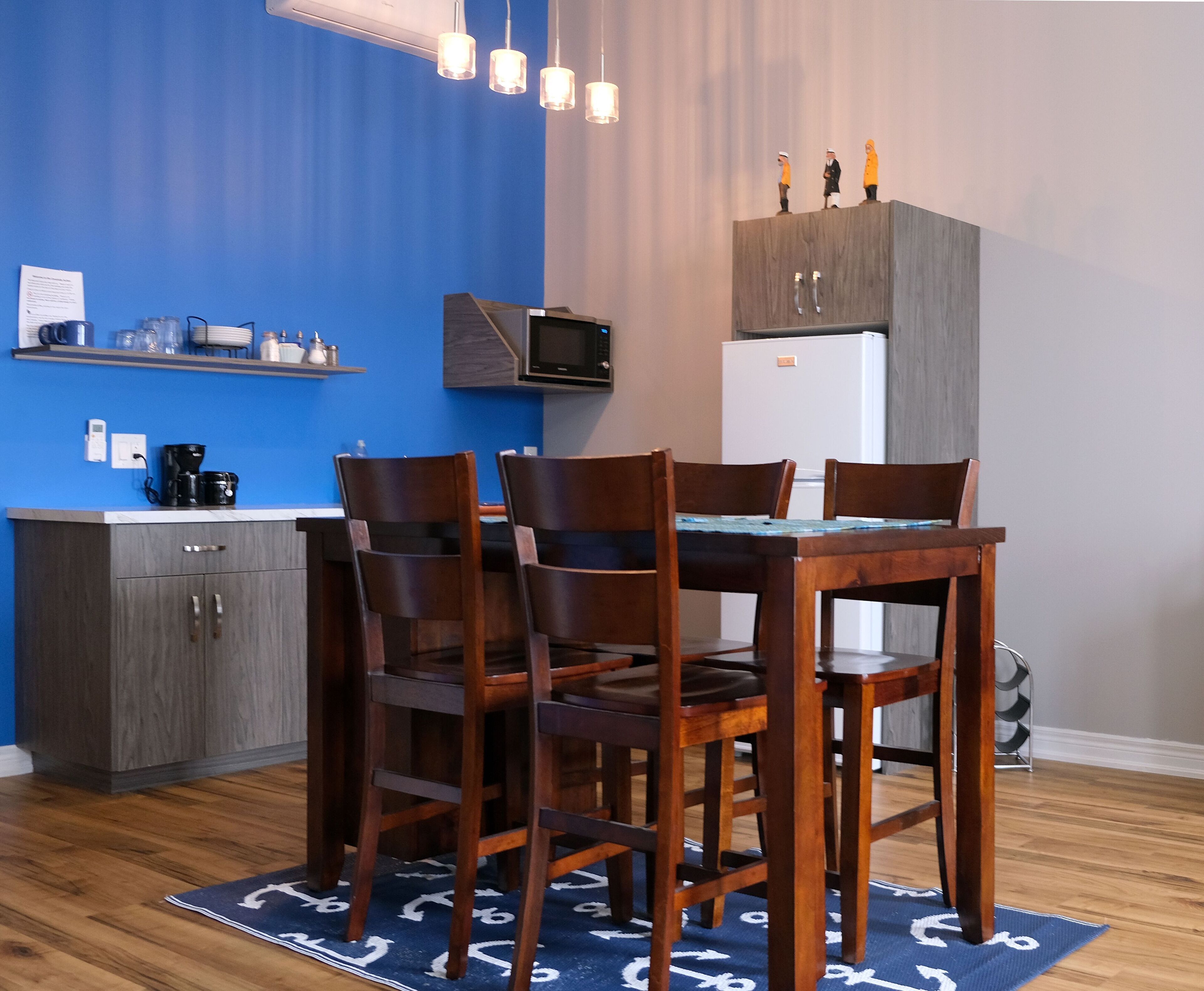 Une cuisine compacte comprenant une table et des chaises, un four à micro-ondes, un réfrigérateur et une étagère où sont rangés les ustensiles de cuisine.