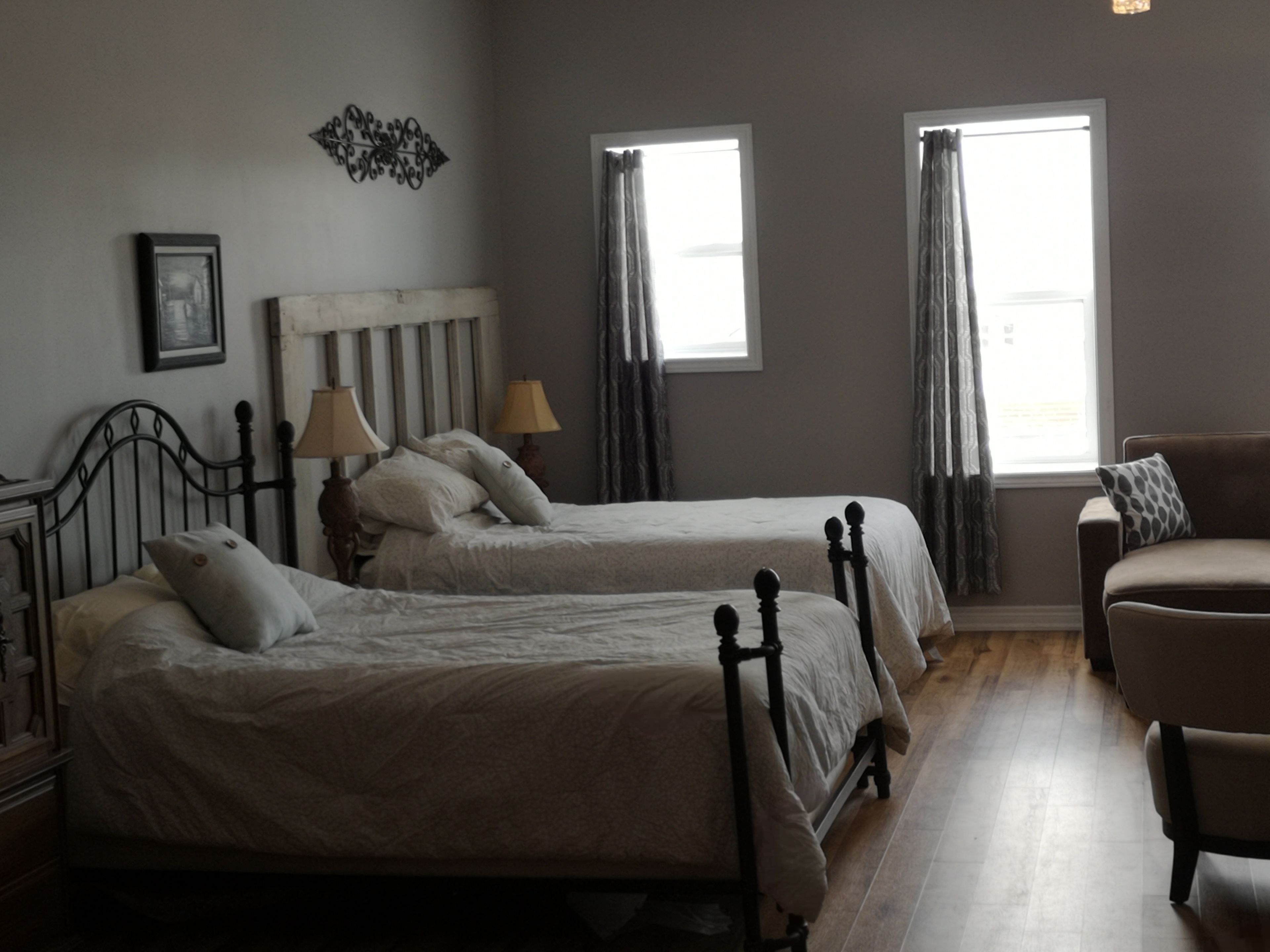 Una camera da letto con due letti singoli, un comodino con una lampada, una sedia e una finestra con tende.