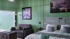 Un dormitorio con cama, un banco, una silla, una mesita y un ventilador de techo.