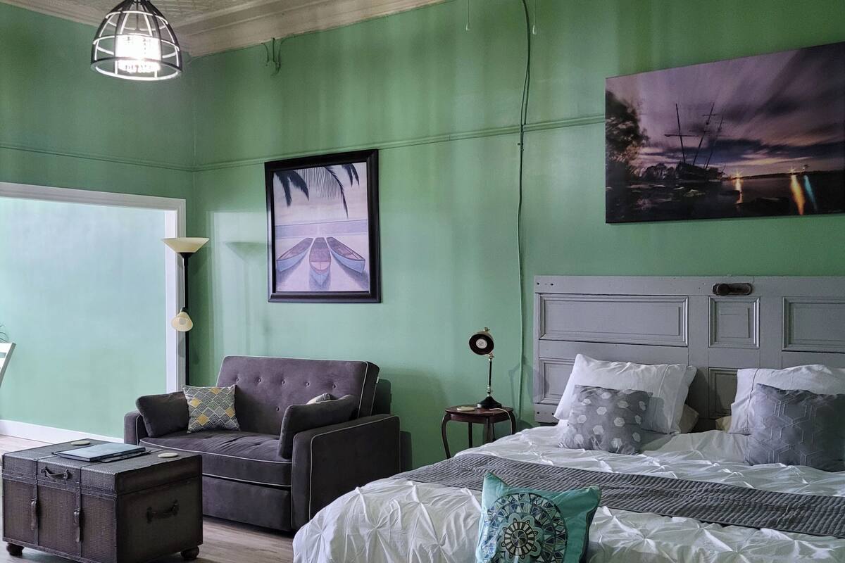 Ein Schlafzimmer mit Bett, einer Bank, einem Stuhl, einem kleinen Tisch und einem Deckenventilator.