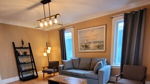 Una sala de estar con sofá, sillones, una mesa de centro, una estantería y un cuadro en la pared.