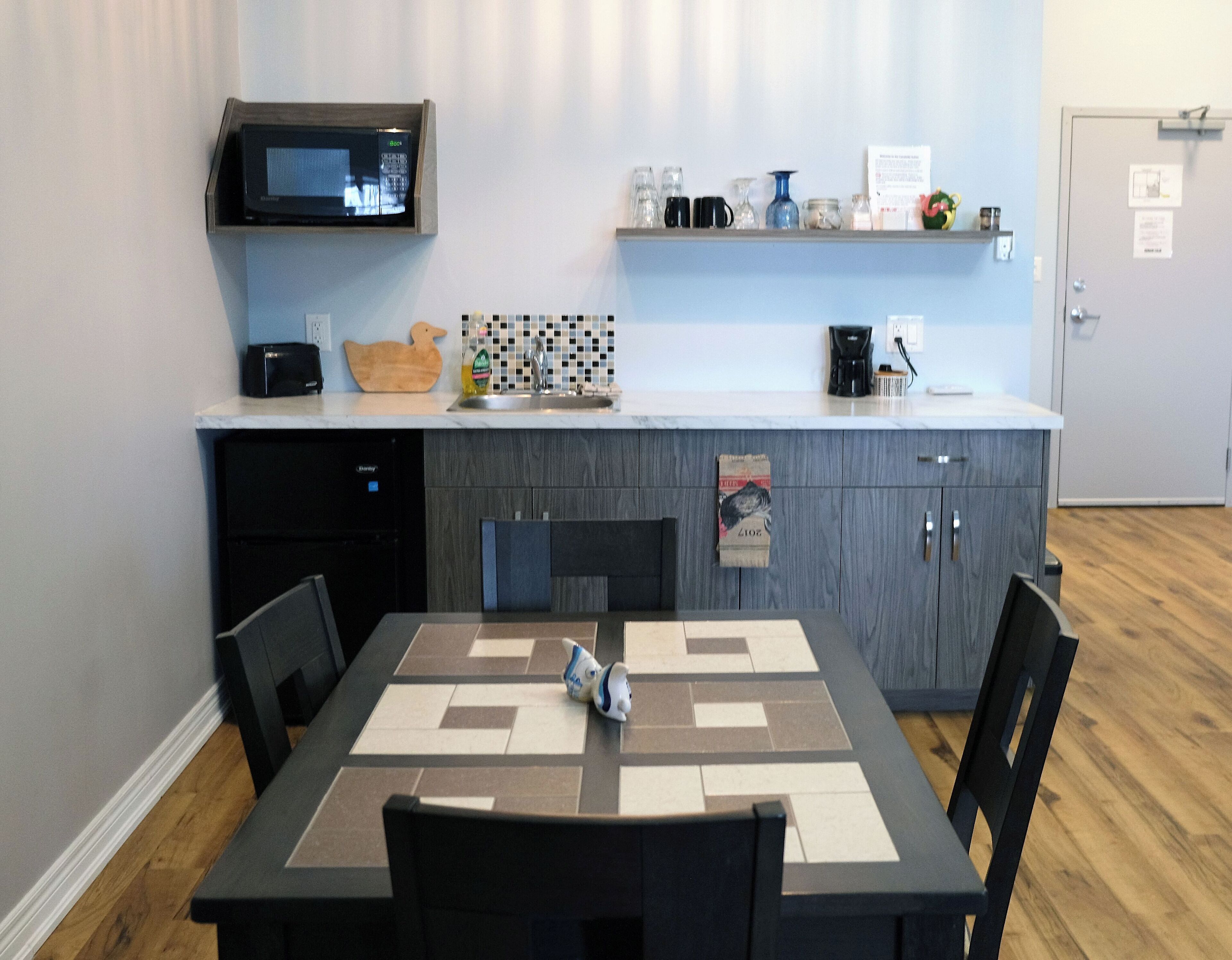 Una cocina moderna con microondas, cafetera y una pequeña estantería con diversos objetos.