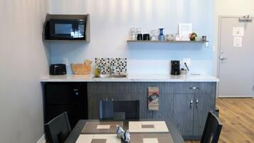 Una cocina moderna con microondas, cafetera y una pequeña estantería con diversos objetos.