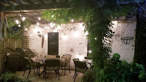 Eine Terrasse im Freien mit Steinboden, einem Tisch und Stühlen sowie Lichterketten.