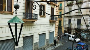 Une rue étroite, avec les volets des magasins baissés, un fourgon blanc garé sur le côté droit, et une personne qui marche.