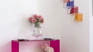 Un comptoir d’accueil orné d’un vase de fleurs, une pancarte indiquant « Accueil », et un ensemble d’étagères colorées et transparentes sur lesquelles sont disposées des figurines.