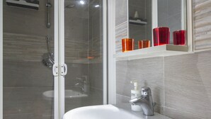 Une salle de bain avec une douche à parois de verre, un lavabo blanc doté d’un distributeur de savon et un miroir au-dessus du lavabo.