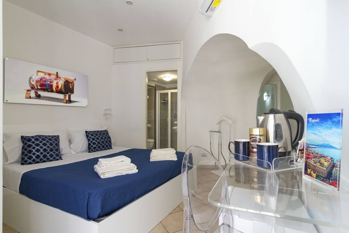 A hotel room with a bed, a desk with a coffee maker, and a framed picture on the wall.