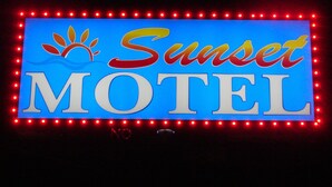 A neon sign for Sunset Motel with a stylized sun and palm tree. - Sunset Motel (Taft)
