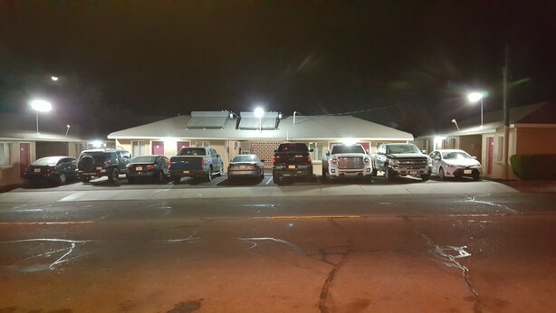 A parking lot with several vehicles parked in front of a building with a flat roof and multiple doors. - Sunset Motel (Taft)