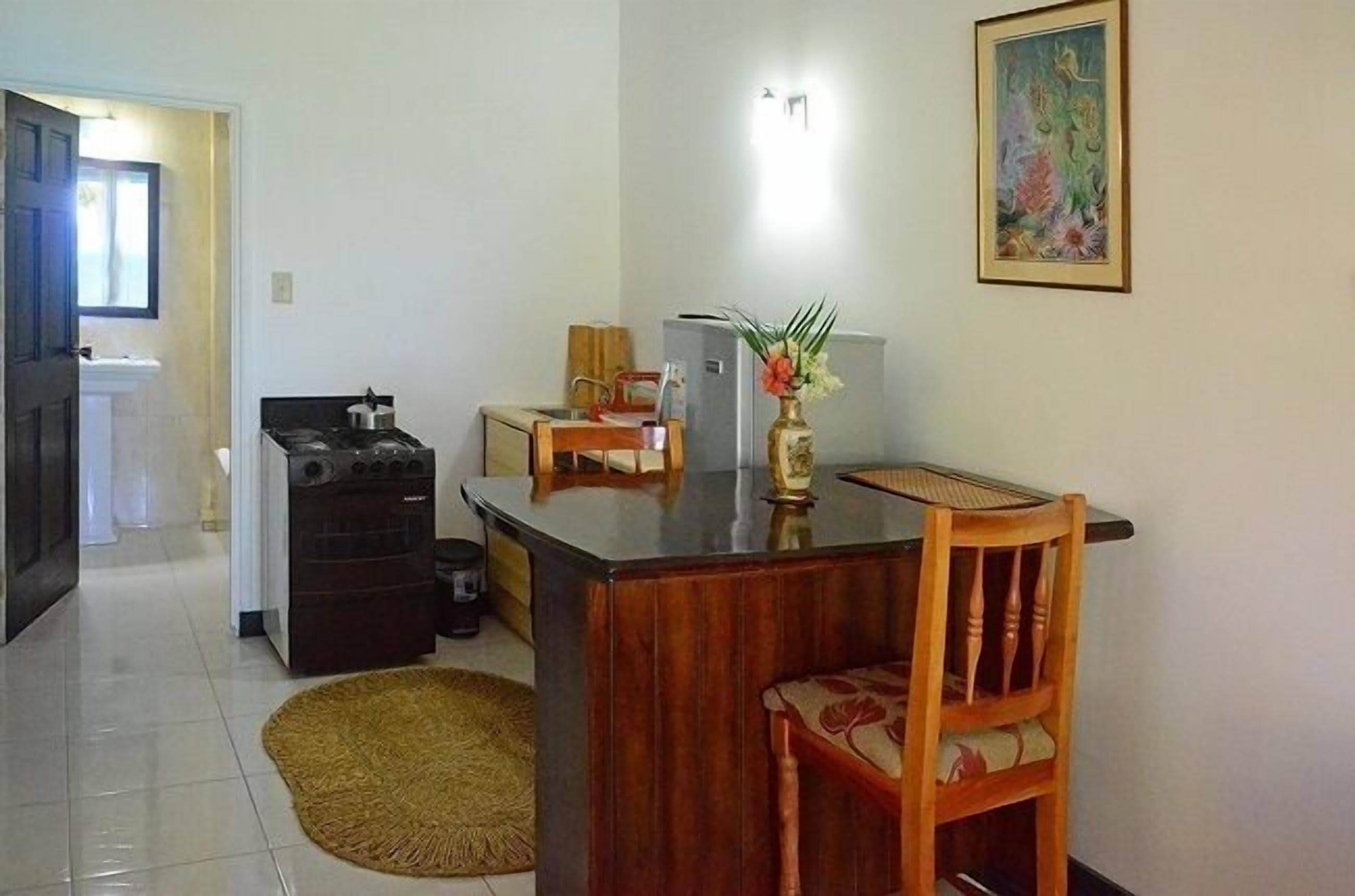 A compact kitchen with a refrigerator, stove, and sink. A dining table with chairs is positioned in front of the kitchen.