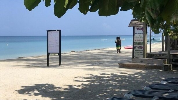 A beach with lounge chairs and a signboard. - Firefly Beach Cottages and Suites (Negril)