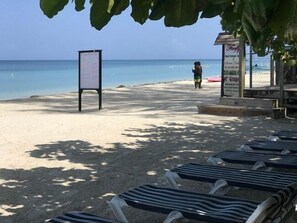 A beach with lounge chairs and a signboard.