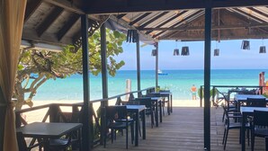 An outdoor dining area with tables and chairs, overlooking a beach with a clear view of the ocean and a boat in the distance. - Firefly Beach Cottages and Suites (Negril)