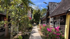 A narrow pathway flanked by wooden buildings with hanging baskets and vibrant pink flowers. - Firefly Beach Cottages and Suites (Negril)