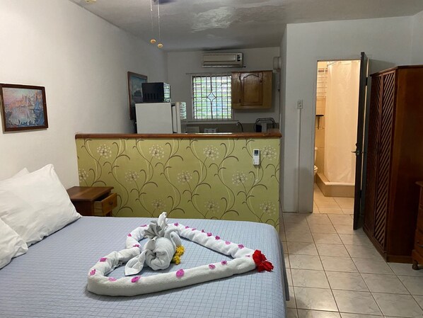 A hotel room with a bed, a small desk, a kitchenette, and a bathroom.