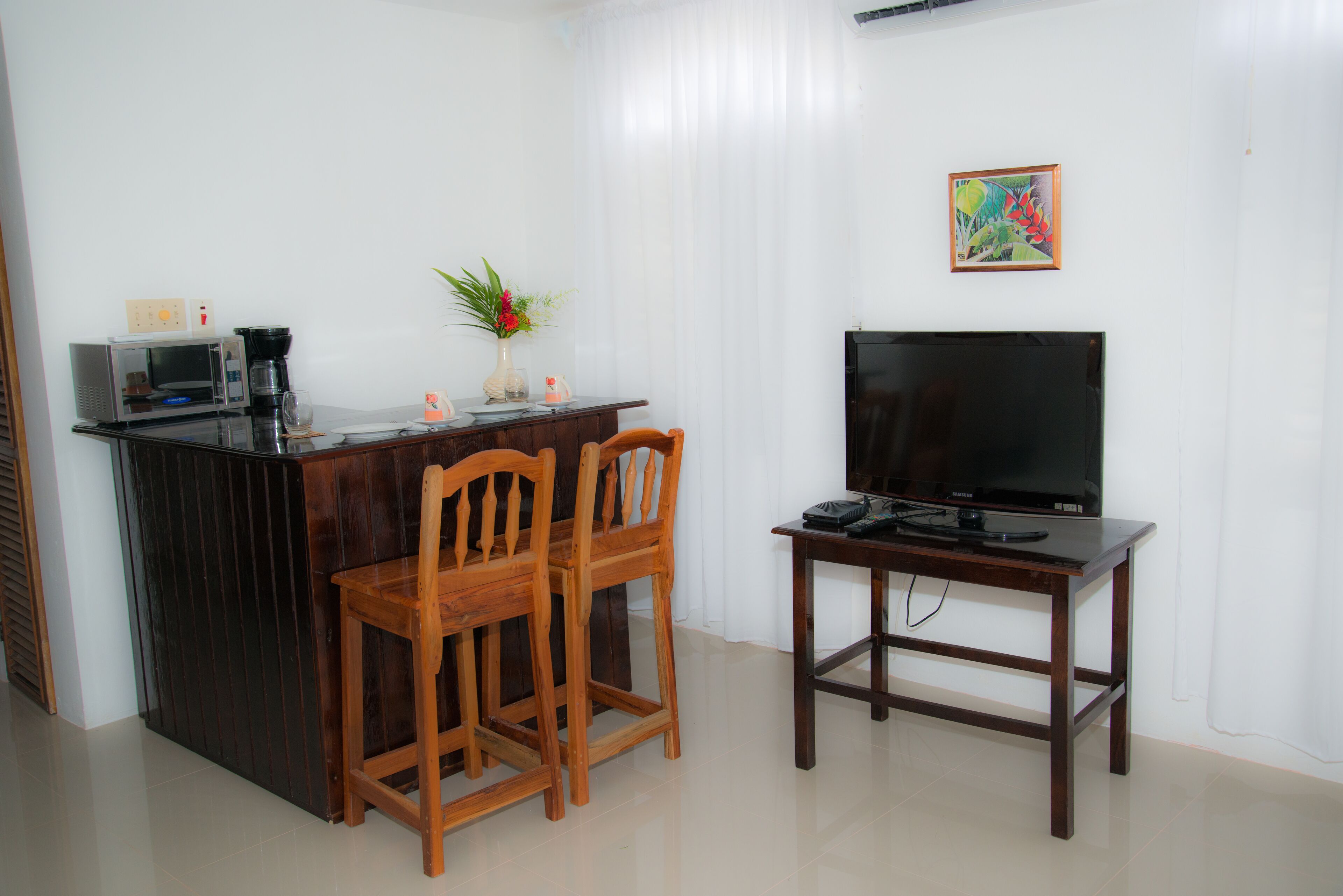 Un espacio habitable compacto con kitchenette, una zona de comedor con dos sillas de madera, una pequeña mesa de madera y un televisor de pantalla plana.