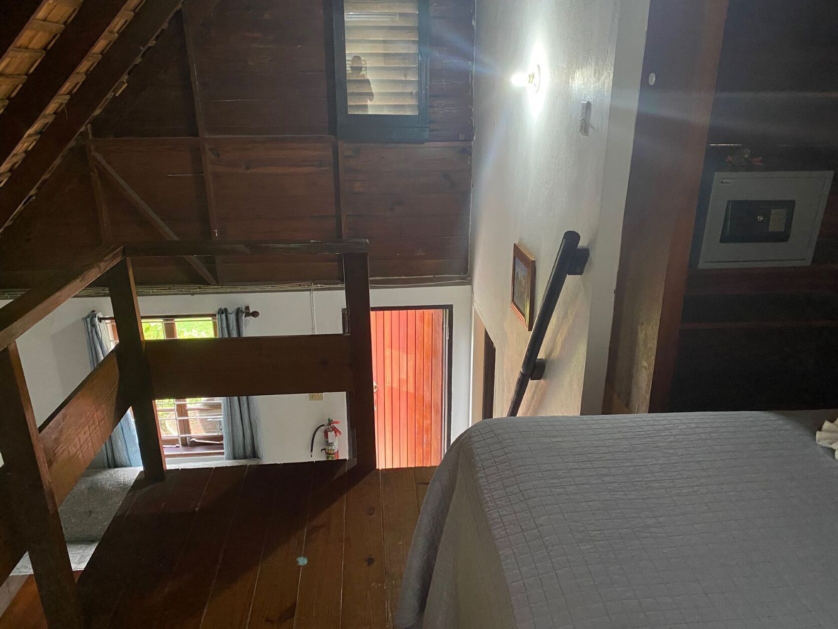 Una habitación con techos altos, una escalera de madera, una cama y un ventanal con persianas.