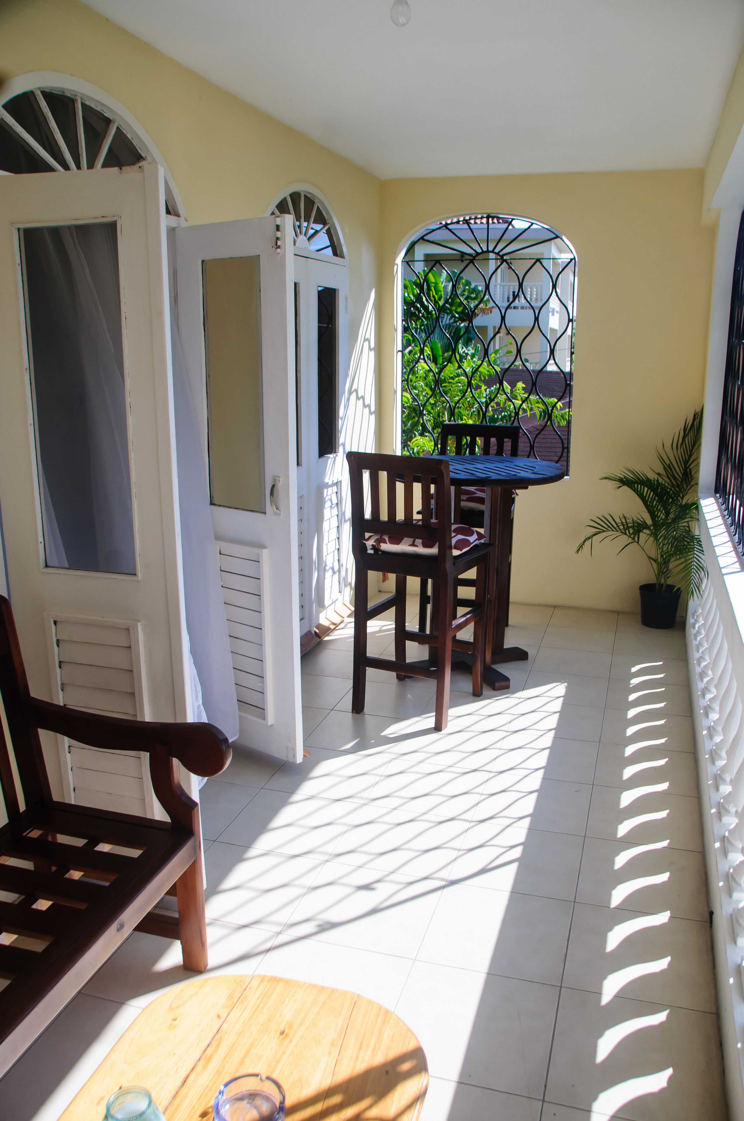 A balcony with a table and chairs, a potted plant, and a view of greenery through a window.