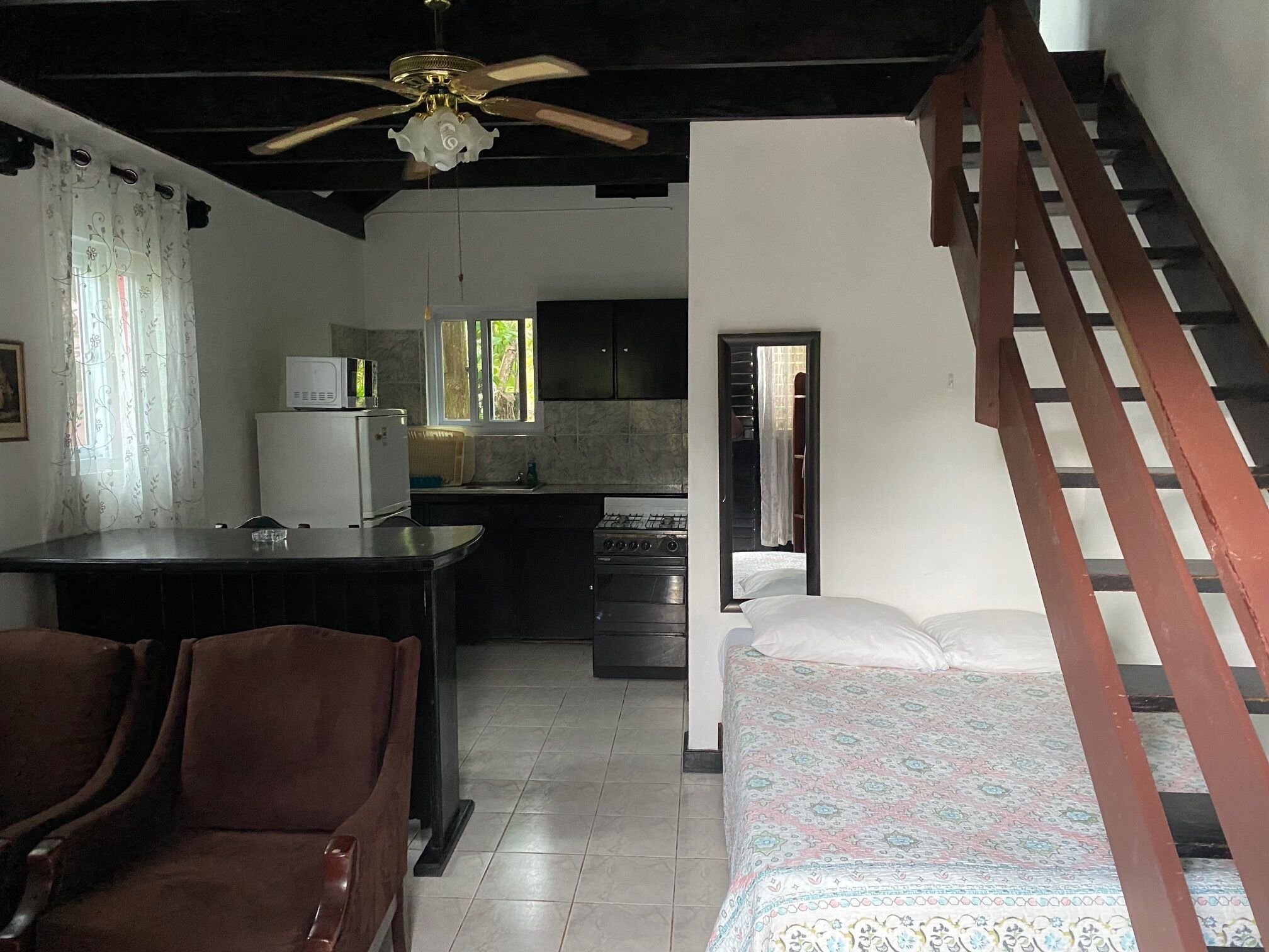 A compact living space with a kitchenette, a dining area with chairs, a bed, and a staircase.