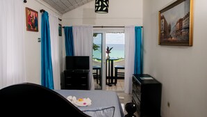 A hotel room with a bed, a TV, a desk, and a balcony with a view of the sea. - Firefly Beach Cottages and Suites (Negril)